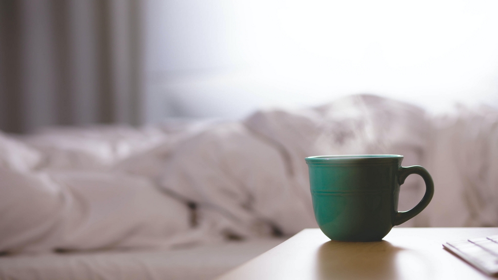 A relaxing scene with a cup of ginseng tea placed on a tray in bed.